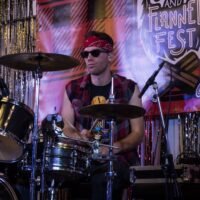 drummer in red flannel vest smirking at camera on stage during Wyandotte's Fire & Flannel Festival